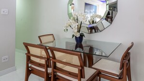 A dining area with a glass table, four wooden chairs, a blue vase with white flowers, and a large hexagonal mirror on the wall. - Acogedor Rinc n en Ipanema Ac2002 (Rio de Janeiro)