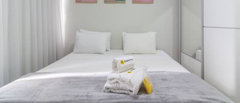 A hotel room with a bed, two pillows, a set of towels, and three framed pictures on the wall.