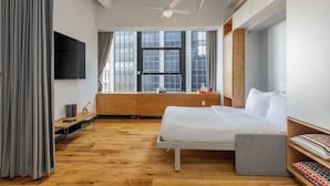 A modern hotel room with a bed, a desk, a TV, and large windows. - Central FiDi Studio Near NYC’s Top Attractions, Dining, and Iconic Landmarks (New York)