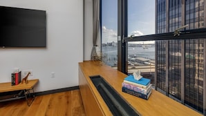 A modern room with a large window overlooking a cityscape and water. - Central FiDi Studio Near NYC’s Top Attractions, Dining, and Iconic Landmarks (New York)