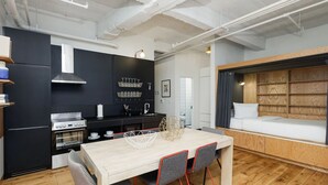 A modern kitchen with black cabinets, a wooden dining table, and a built-in bed with a wooden headboard. - Relax in a Modern Apartment Within Walking Distance to Wall Street Subway (New York)