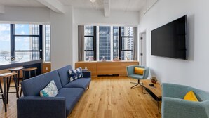 A modern living room with a sofa, armchairs, a TV, and a dining area with stools.
