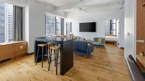 A modern living space with a kitchen island, bar stools, a sofa, and a flat-screen TV.