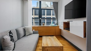 Een moderne woonkamer met een grijze bank, een houten salontafel en een grote televisie aan de muur.