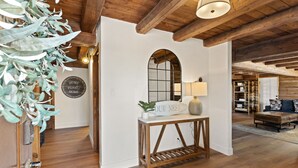 A wooden interior with a white wall, a wooden table with a sign, a lamp, and a mirror.