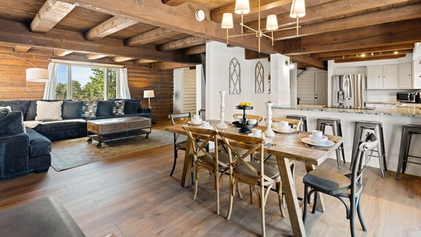 A spacious living area with a wooden ceiling, a dining table with chairs, and a kitchen in the background.
