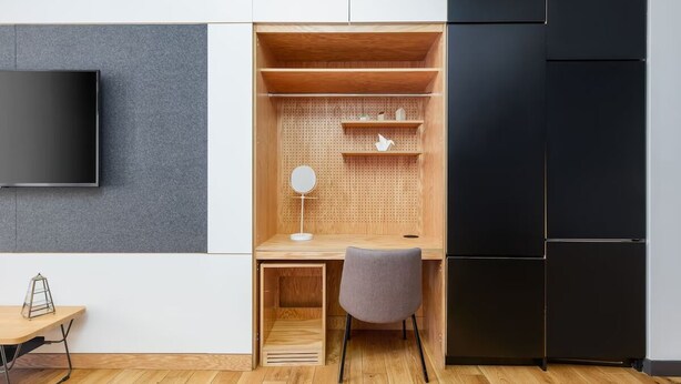 Une chambre moderne avec un bureau en bois, une chaise grise, un téléviseur à écran plat et un meuble noir.