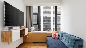 Un salon moderne doté d’un grand téléviseur à écran plat, d’un meuble en bois, d’un canapé bleu et d’une fenêtre donnant sur la ville.