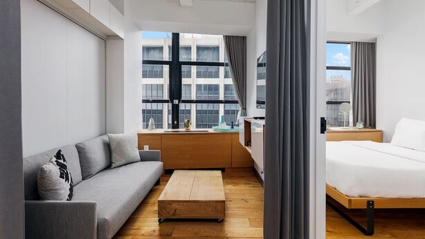 Una moderna camera d'albergo con un divano, un tavolino in legno, un letto e vista sulla città attraverso ampie finestre.
