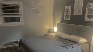 Un dormitorio con cama, ventilador de techo, mesita de noche, lámpara y cuadros en la pared.