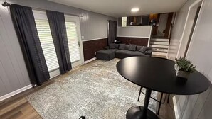 Un espacio habitable compacto con un sofá modular, una mesa de comedor redonda y una zona de cocina al fondo.