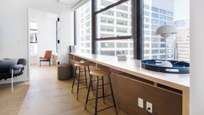 A modern kitchen with a large window, wooden bar stools, and a round table with a lamp. - Relax in a Modern Apartment | Walking Distance to Wall Street Subway (New York)