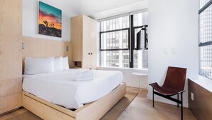 A modern bedroom with a wooden bed, a large window, a chair, and a painting on the wall. - Stylish Apartment in Manhattan | Ideal for Long Stays & City Exploring (New York)