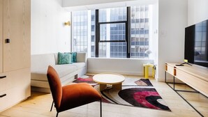 A modern living room with a sofa, a round coffee table, a vibrant rug, and a TV. - Vibrant Studio Near South Street Seaport & Multiple Dining Options (New York)