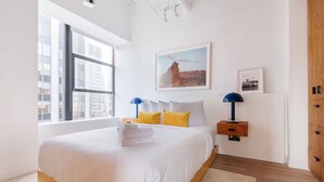Une chambre d’hôtel moderne avec un grand lit, une fenêtre donnant sur la ville, une armoire en bois et un tableau encadré au mur.