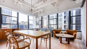 Un espace de bureau moderne avec une grande table en bois, des chaises en osier et un coin salon avec un canapé.