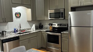 A modern kitchen with grey cabinets, stainless steel appliances, and a wooden dining table with star-patterned placemats. - Sunny Daze 1 Bed Apt. (Biloxi)