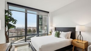 A modern hotel room with a large window, a bed, a bedside table, and a lamp. - Stylish Studio w/ Kitchen & Laundry | Perfect for Long Stays at the Heart of DC (Washington)