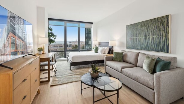 Une chambre d’hôtel moderne équipée d’un lit, d’un canapé, d’une télévision et d’une grande fenêtre donnant sur la ville.