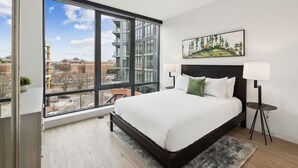 A modern bedroom with a large window, a bed, a nightstand, and a painting on the wall. - Prime City Escape | Spacious Haven w/ Kitchen, Pet & Family Friendly (Washington)