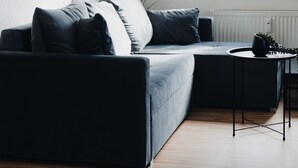 A modern living room with a dark sofa, a small side table, and a window with plants.