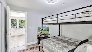 Une chambre avec un lit superposé, un téléviseur posé sur un meuble, une porte donnant sur un balcon et un ventilateur de plafond.