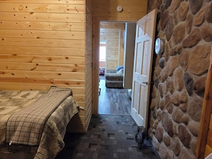 Ein Zimmer in einer Holzhütte mit einem Bett, einem kleinen Tisch und einer Steinwand.