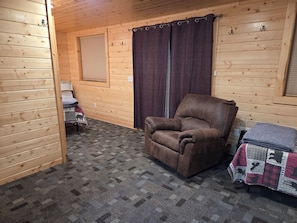 Een interieur van een blokhut met een leren fauteuil, een klein tafeltje met een plaid en een raam met zonwering.
