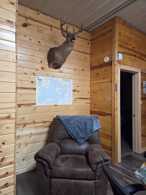 Een houten chalet inrichting met een opgezette hertenkop aan de muur, een kaart en een leren relaxfauteuil.