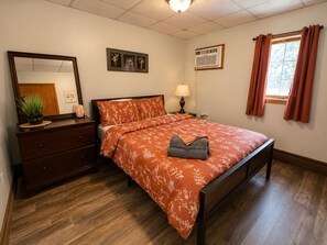 A bedroom with a wooden bed, a dresser, a mirror, a nightstand with a lamp, and a window with curtains.