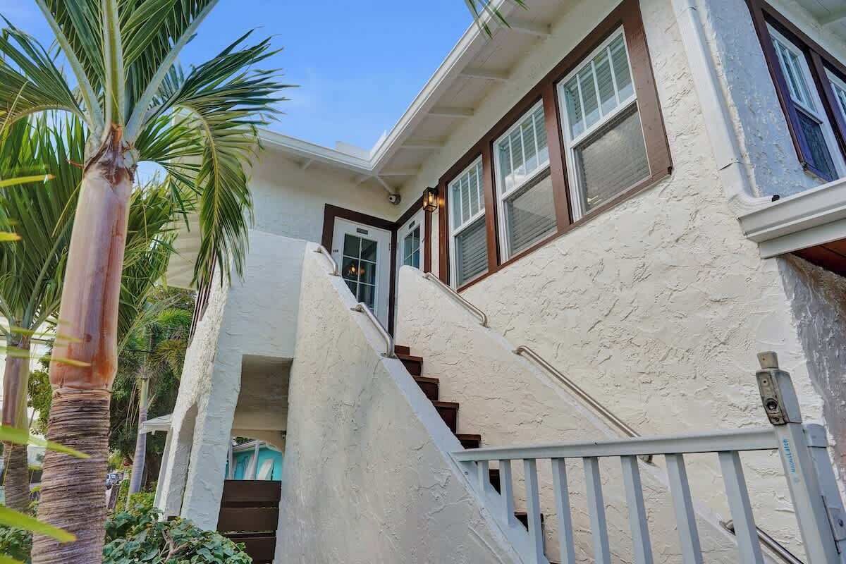 A two-story building with a white exterior, a wooden staircase, and a door leading to the upper floor.