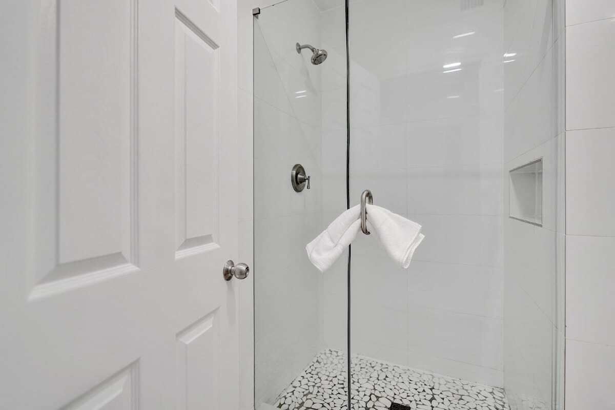 A glass-enclosed shower with a white tiled floor and a white towel hanging on the door.