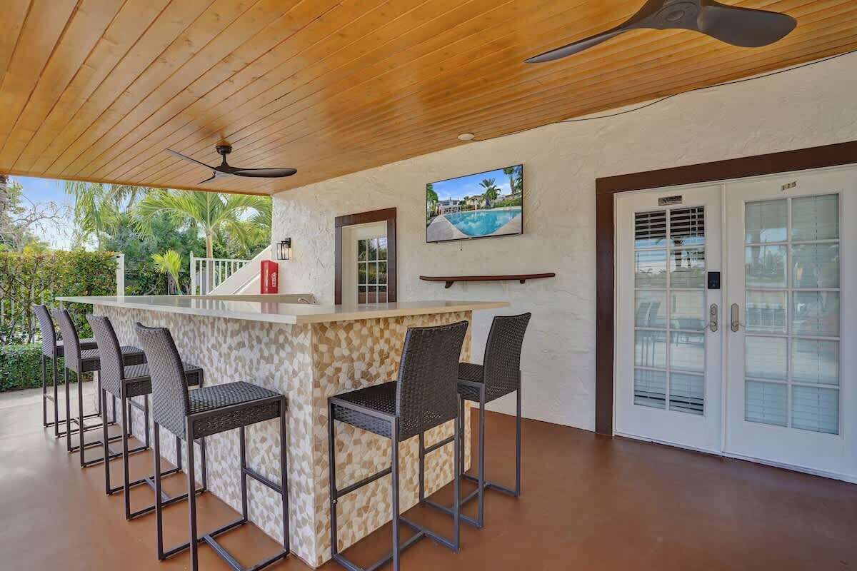 Covered outdoor bar with wicker stools, mounted TV, and ceiling fan — great for entertaining.