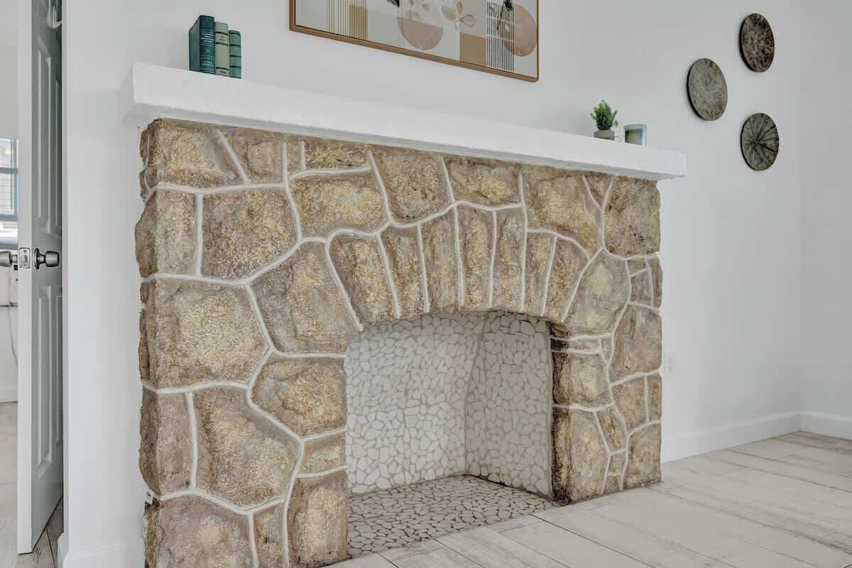 Une cheminée en pierre avec un manteau de cheminée blanc, entourée d’un mur blanc orné d’assiettes décoratives et agrémentée d’une petite plante.