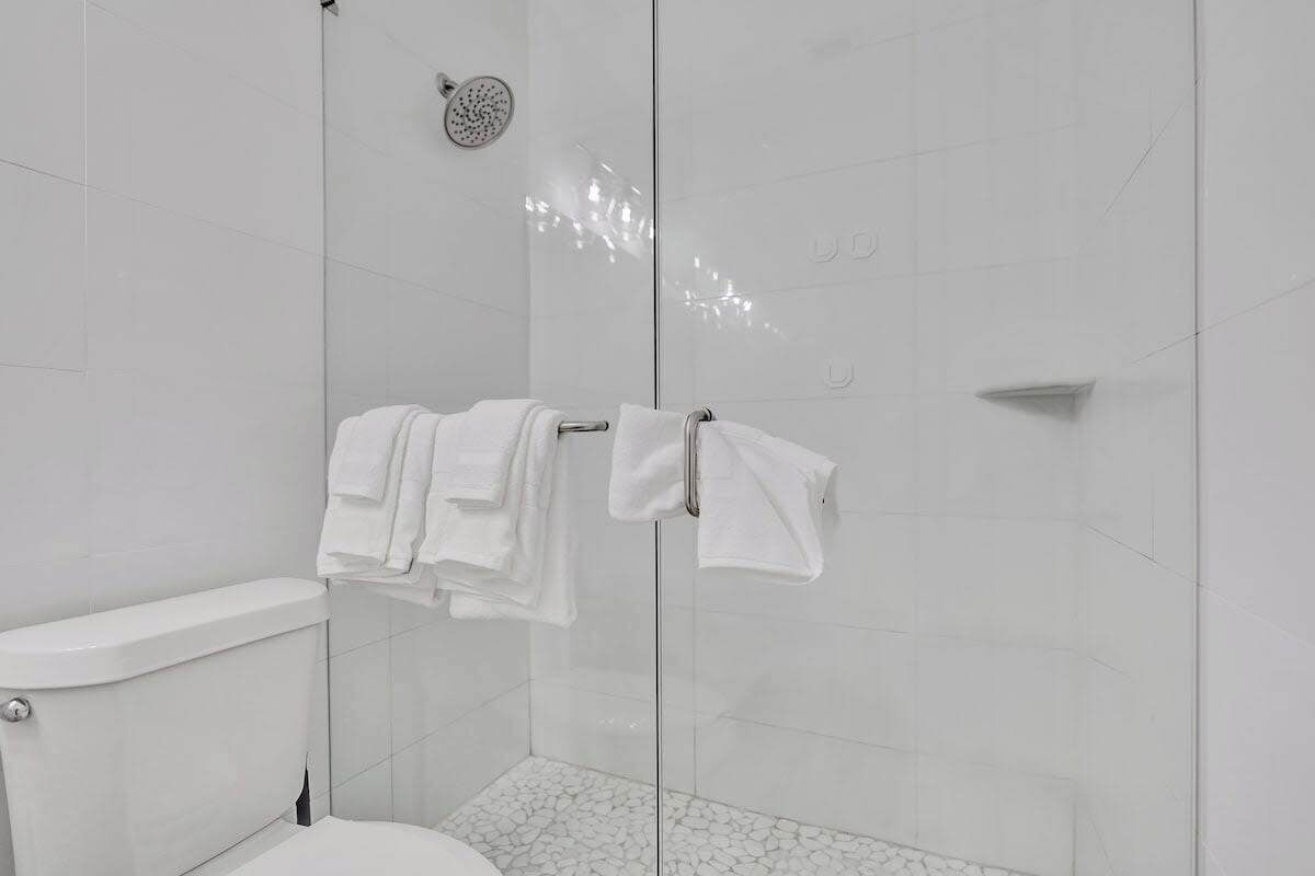 A modern bathroom with a glass shower enclosure, a toilet, and a towel rack with folded towels.