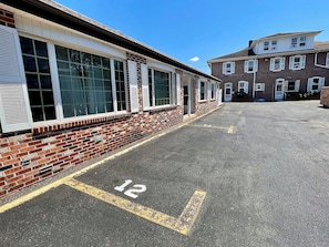 A parking lot with a brick building and a two-story structure in the background.