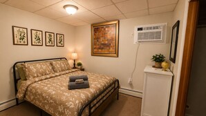 Una camera da letto con un letto, una lampada da comodino, condizionatore d'aria, opere d'arte a parete e un piccolo mobile con un mappamondo.