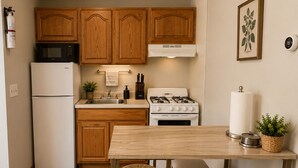 Una cucina compatta con mobili in legno, un frigorifero bianco, un fornello e un forno a microonde. C'è un piccolo tavolo da pranzo con una panca.