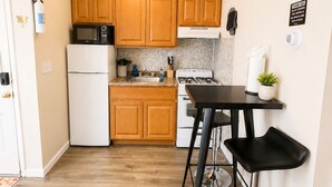 A compact kitchen with wooden cabinets, a microwave, a refrigerator, a stove, and a bar stool. - Cozy 1BR End Cottage W/D • Parking •Walk to Train (Swarthmore)