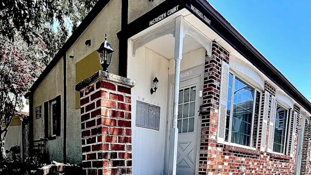 A building with a brick facade, a white door, and a sign reading "Pastuszek Court". - Cozy 1BR End Cottage W/D • Parking •Walk to Train (Swarthmore)