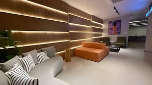 Un interior moderno con un sofá curvo, un pequeño sofá naranja y una pared con paneles iluminados.
