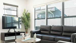 Una sala de estar moderna con un sofá de cuero negro, un televisor de pantalla plana sobre un mueble negro y una mesa redonda de centro con adornos.