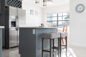Eine moderne Küche mit einem Edelstahlkühlschrank, einer grauen Kücheninsel mit Barhocker und einem großen Fenster, das natürliches Licht hereinlässt.
