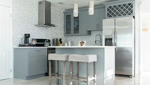 Una cocina moderna con armarios grises, un refrigerador de acero inoxidable y dos taburetes de bar.