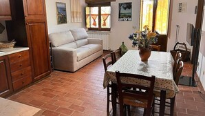 Ein gemütlicher Wohnbereich mit Sofa, Esstisch und Stühlen, einer Küchenzeile mit Schränken und einem Fenster mit Vorhängen.