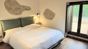 Een slaapkamer met een groot bed, decoratieve stenen wanden, een nachtkastje met lamp en uitzicht door een glazen deur.