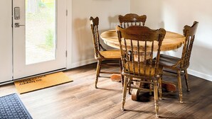 Un coin repas avec une table ronde en bois, quatre chaises, un lustre suspendu et deux tableaux encadrés au mur.