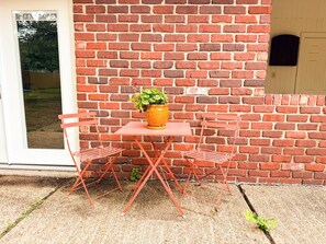 Eine Ziegelwand, eine Tür, ein Fenster und ein Tisch mit Stühlen und einer Topfpflanze.