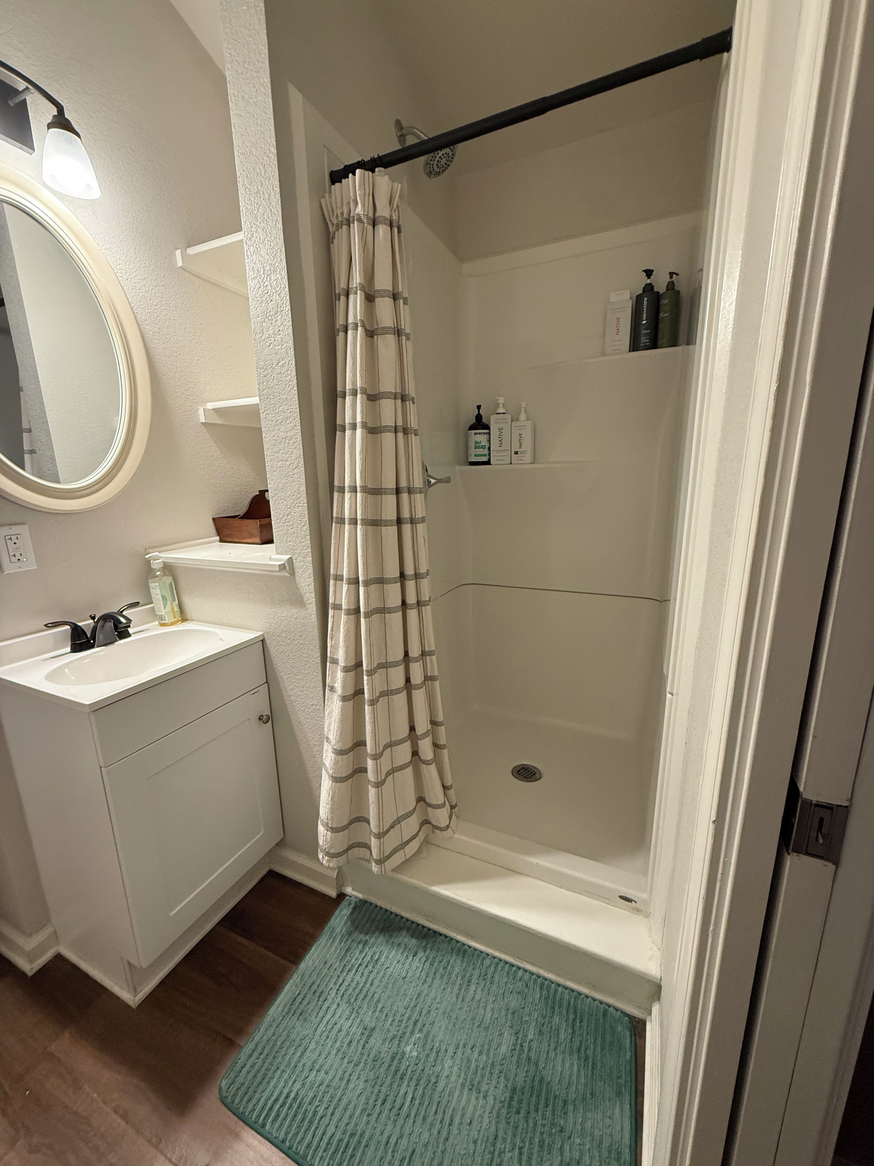 A bathroom with a shower, a sink, a mirror, and toiletries on a shelf.