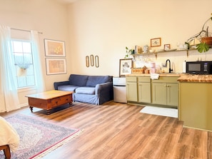 Una sala de estar con sofá, una mesa de centro, una zona de cocina con microondas y refrigerador.